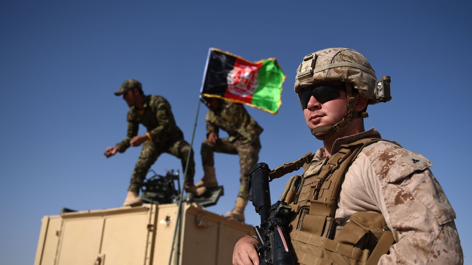 In this photograph taken on August 28, 2017, a US Marine looks on as Afghan National Army soldiers raise the Afghan National flag on an armed vehicle during a training exercise to deal with IEDs (improvised explosive devices) at the Shorab Military Camp in Lashkar Gah in Helmand province. - Marines in Afghanistan's Helmand say Donald Trump's decision to keep boots on the ground indefinitely gives them all the time in the world to retake the province, once the symbol of US intervention but now a Taliban stronghold. They may need it. At the hot, dusty Camp Shorab, where many of the recently deployed Marines train their Afghan counterparts in flat, desert terrain, the Afghans admit th - اسپوتنیک افغانستان  , 1920, 02.01.2022
