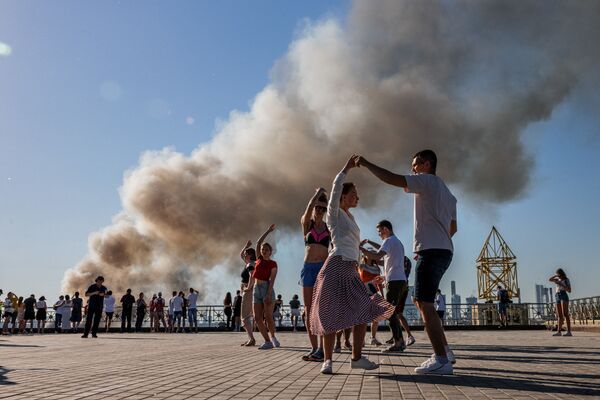 زوج ها همزمان با برخاستن دود از یک انبار تولید مواد شیمیایی در مسکو، سامبا می رقصند. - اسپوتنیک افغانستان  