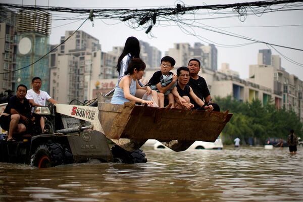 Люди едут на фронтальном погрузчике, пробираясь через паводковые воды после проливوقوع سیل ویرانگر در چین.ных дождей в Чжэнчжоу, провинция Хэнань, Китай - اسپوتنیک افغانستان  