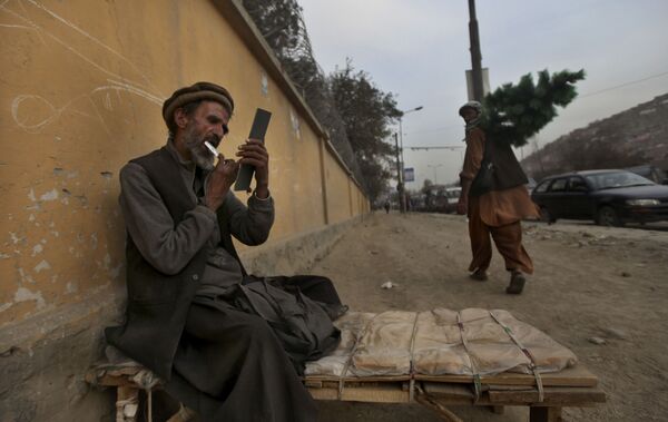 یک آرایشگر خیابانی در کابل سال 2010 در حالی که منتظر مشتری است، ریش خود را اصلاح می‌کند. - اسپوتنیک افغانستان  