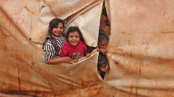 Сирийские дети выглядывают из палатки, оборудованной под класс, в лагере беженцев на границе с Турцией в провинции Идлиб - اسپوتنیک افغانستان  