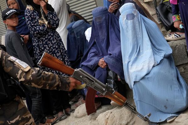 طالب مسلح در برابر زنان برقع پوش که منتظر دریافت جیره غذایی برای کودکان شان هستند. - اسپوتنیک افغانستان  