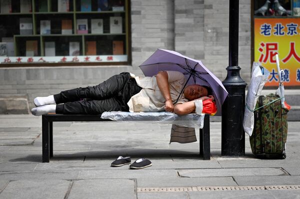 مردی در امتداد جاده ای در پکن در حالی که در زیر چتر پناه گرفته است، روی یک دراز چوکی به خواب رفته است. - اسپوتنیک افغانستان  