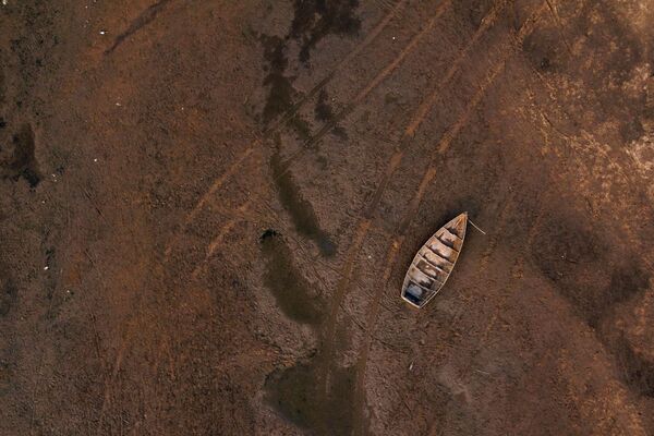 نمای هوایی از ردهای یک وسیله نقلیه در بستر رودخانه در کنار یک قایق سرگردان در رودخانه خشک پارانا، که سطح آب آن به پایین ترین سطح تاریخی رسیده است، در طول یک خشکسالی تاریخی در گویا، کورینتس، آرژانتین، 21 اگست سال 2021 میلادی - اسپوتنیک افغانستان  