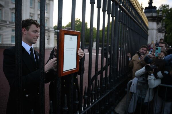 مردم درحال خواندن مرگ ملکه دوم بریتانیا در دروازه ورودی قصر. - اسپوتنیک افغانستان  