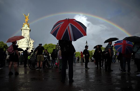 مردم زیر باران با چتری که بیرق بریتانیا در او نصبب شده، در نزدیکی قصر ملکه بریتانیا جمع شده اند.  - اسپوتنیک افغانستان  