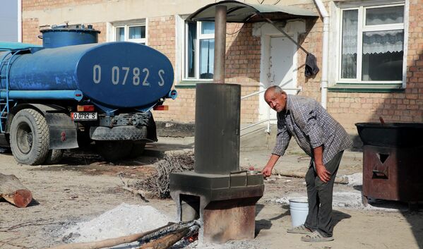 مهاجر قرغیزستان در یکی از کوچه های قریه بوز آدیر آب را جوش میدهد. - اسپوتنیک افغانستان  