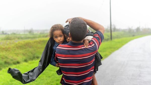 Мужчина несет двоих детей под дождем в поисках убежища после того, как ураган Иэн затопил их дом в Пинар-дель-Рио, Куба - اسپوتنیک افغانستان  