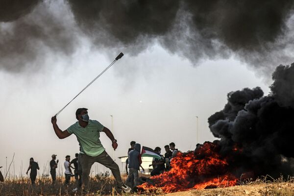 یک معترض فلسطینی در 25 اکتوبر 2022 در جریان درگیری با نیروهای اسرائیلی پس از تظاهرات در امتداد مرز، از یک پلخمان برای پرتاب سنگ به آن سوی مرز با اسرائیل در شرق شهر غزه استفاده می کند. (عکس از محمود حمس / خبرگزاری فرانسه) - اسپوتنیک افغانستان  