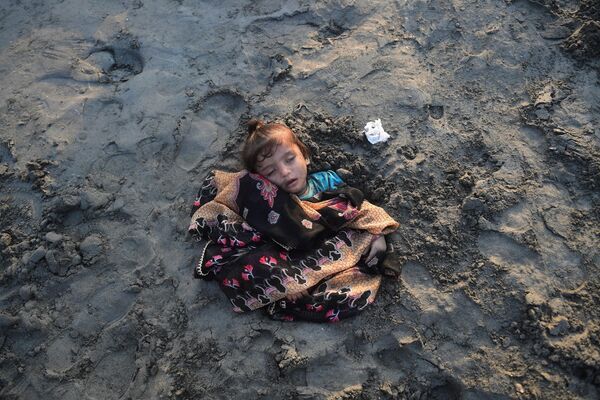 دختری در حال خواب کردن،این دختر از سوی پدر و مادرش با شن در ساحل پوشیده شده است. مادر و پدر این دختر به این باوراند، که قرار گرفتن در معرض خورشید گرفتگی بیماری دخترشان را التیام می بخشد، در کراچی در 25 اکتوبر 2022. (عکس از آصف حسن / خبرگزاری فرانسه) - اسپوتنیک افغانستان  