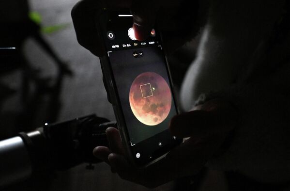 مردی با استفاده از گوشی هوشمند از یک ماه خونی از طریق تلسکوپ در طول ماه گرفتگی کامل در گویانگ، شمال غربی سئول، در 8 نوامبر 2022 عکس می گیرد. - اسپوتنیک افغانستان  