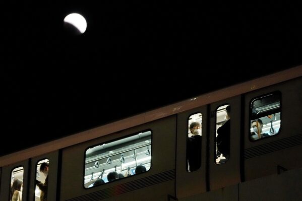 مردم در هنگام ماه گرفتگی بر فراز آسمان توکیو در روز سه شنبه، 8 نوامبر 2022، سوار قطار می شوند. - اسپوتنیک افغانستان  
