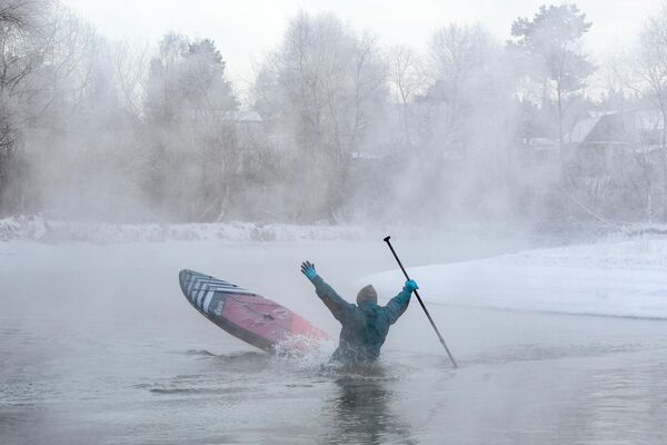 یک ورزشکار از گروه SUP-Novosibirsk در طول یک شنا زمستانی در رودخانه ای بدون یخ در نزدیکی نووسیبیرسک. برای تمرینات زمستانی از لباس های مرطوب خشک استفاده می شود که در صورت افتادن در آب لباس خیس را حذف می کند. - اسپوتنیک افغانستان  
