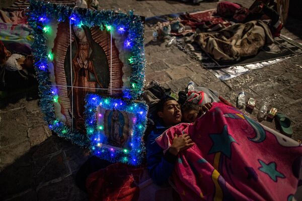 زن و شوهری در کنار تصاویر باکره گوادالوپ در آنجا استراحت می کنند و با دیگر زائران خارج از کلیسای گوادالوپ در مکزیکوسیتی اردو می زنند.  مکزیکی ها ظهور باکره گوادالوپ به خوان دیگو در سال 1531 را گرامی می دارند. (عکس از نیکلاس عصفوری / خبرگزاری فرانسه) 11 دسامبر 2022 - اسپوتنیک افغانستان  