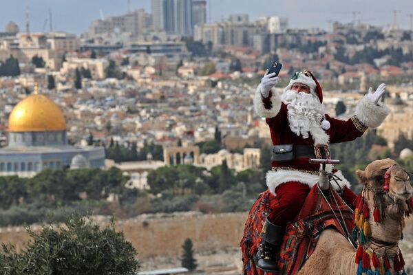 عیسی کاسیسیه فلسطینی، با لباس بابا نوئل، در حالی که سوار بر شتر در کوه الویا در یورسلیم، چند هفته قبل از تعطیلات  کریسمس در 6 دسامبر 2022، عکس می گیرد. - اسپوتنیک افغانستان  