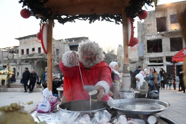 یک مرد سوری با لباس بابا نوئل در یک بازار کریسمس در میدان الحطب در شمال شهر حلب سوریه، شیری شیرین به نام سهلاب می فروشد.  24 دسامبر 2022 - اسپوتنیک افغانستان  