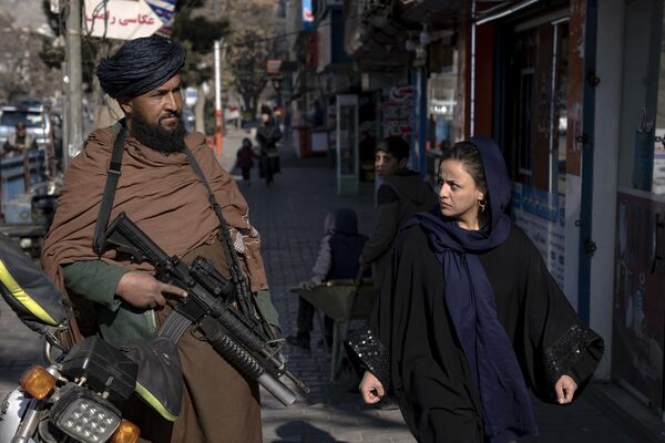 یک جنگجوی طالبان در حالی که زنی در کابل، افغانستان در حال راه رفتن است، نگهبانی می‌دهد.احکام اخیر طالبان در مورد زنان افغان شامل ممنوعیت تحصیل در دانشگاه و کار برای سازمان های غیردولتی است که باعث اعتراض در شهرهای بزرگ شده است.حضور نیروهای امنیتی در کابل پایتخت در روزهای اخیر تشدید شده است و پوسته های بیشتر، خودروهای مسلح و نیروهای ویژه طالبان در خیابان ها حضور دارند. مقامات دلیلی برای تدابیر شدیدتر امنیتی ارائه نکرده اند.دوشنبه، 26 دسامبر 2022 - اسپوتنیک افغانستان  