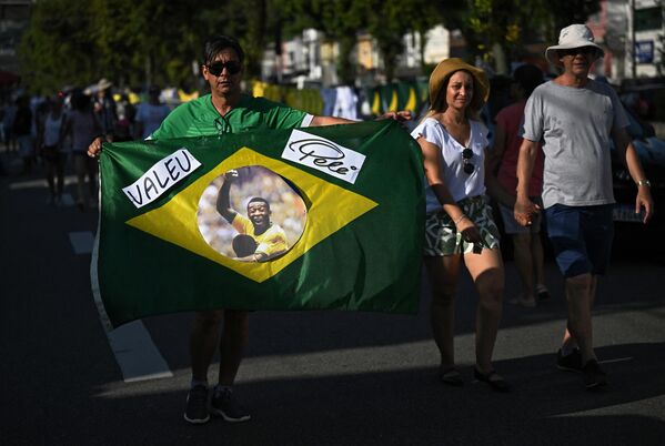 یک عزادار پرچم برزیل را با چهره پله اسطوره فوتبال برزیل در خارج از استادیوم اوربانو کالدیرا، که با نام ویلا بلمیرو نیز شناخته می شود، در سانتوس، ایالت سائوپائولو، برزیل، به نمایش می گذارد.2 جنوری2023 - اسپوتنیک افغانستان  
