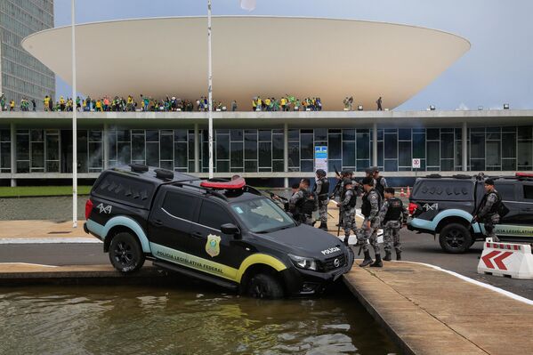 اعضای پلیس قانونگذاری فدرال در کنار موتری ایستاده اند که در حالی که حامیان ژایر بولسونارو، رئیس جمهور سابق برزیل به کنگره ملی در برازیلیا حمله کردند، با یک فواره آب برخورد کرد. - اسپوتنیک افغانستان  