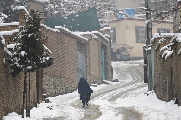 یک خانم در حالی که برقع به سر دارد در کوچه ای برفی در حال راه رفتن است.11 جنوری 2023 - اسپوتنیک افغانستان  