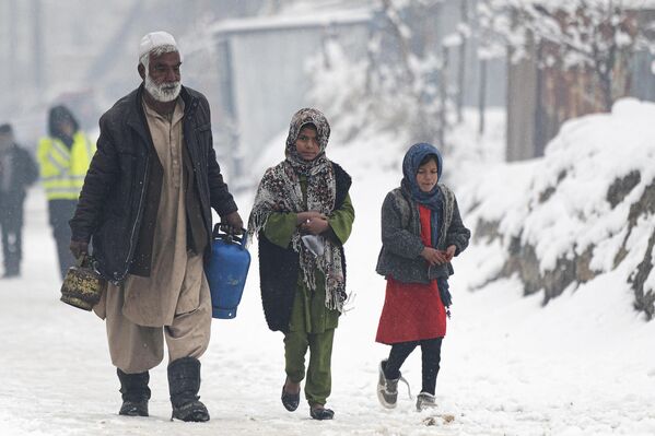 مردی که کپسول های گاز حمل می کند در هنگام بارش برف در کابل در 11 جنوری 2023 در کنار کودکان در امتداد خیابان راه می رود. (عکس از وکیل کوهسار / خبرگزاری فرانسه) - اسپوتنیک افغانستان  