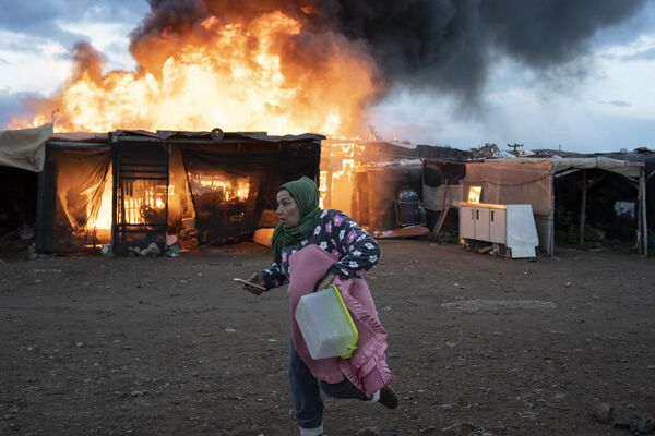 زنی در حین آتش سوزی قبل از اخراج توسط افسران پلیس در آلمریا، اسپانیا، دوشنبه، 30 جنوری 2023، از کنار کلبه های در حال سوختن می دود.یک کمپ مهاجران در شهر نیجار در جنوب اسپانیا که قرار بود روز دوشنبه تخریب شود، آتش گرفت.بیش از 400 نفر در آنجا زندگی می کنند که بسیاری از آنها به عنوان کارگر موقت در زمین های کشاورزی کار می کنند.(AP Photo/Santi Donaire) - اسپوتنیک افغانستان  
