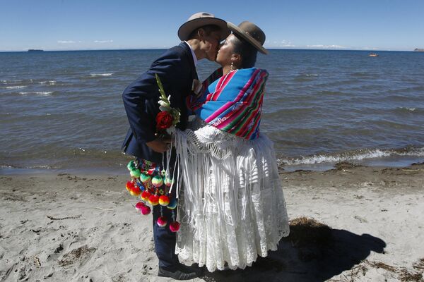 برایان روزل اکوادوری و همسرش ماگدالنا لانکه - که بیش از یک سال پیش از طریق رسانه های اجتماعی با یکدیگر آشنا شدند، پس از ازدواج در طی یک مراسم عروسی دسته جمعی که در آن پنجاه زوج در ساحل دریاچه تیتیکاکا در منطقه آیمارا آکورا در پونو، پرو با هم ازدواج کردند.این اقدام عمومی توسط شهرداری محلی سازماندهی شد و با استفاده از ترکیبی از آداب و رسوم مدرن و اجدادی آند، از جمله حضور یاتیری (شمن) بومی آنها که برای آرزوی خیر برای زوج ها به Pachamama (زمین مادر) پرداخت کرد، برگزار شد.این عکس در 20 اوت 2022، گرفته شده است. - اسپوتنیک افغانستان  
