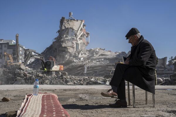 محمت نصیر دوران، 67 ساله، روی صندلی نشسته است، در حالی که ماشین آلات سنگین آوارهای ساختمانی را که پنج نفر از اعضای خانواده اش در نورداگی، جنوب شرقی ترکیه در آن گیر افتاده اند، برمی دارند.هزاران نفر که در یک زلزله فاجعه‌بار خانه‌های خود را از دست دادند، سه روز پس از زلزله و پس‌لرزه‌های متوالی که ترکیه و سوریه را درنوردید، دور آتش‌ها جمع شدند و در سرمای شدید برای غذا و آب غوغا کردند.این عکس پنجشنبه، 9 فوریه 2023، گرفته شده است.(عکس/پطروس جیاناکوریس) - اسپوتنیک افغانستان  