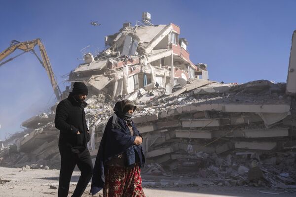 ساکنان محلی در مقابل ساختمان ویران شده در نورداغی، جنوب شرقی ترکیه، پنجشنبه، 9 فبروری 2023 قدم می زنند.هزاران نفر که در یک زلزله فاجعه‌بار خانه‌های خود را از دست دادند، سه روز پس از زلزله و پس‌لرزه‌های متوالی که ترکیه و سوریه را درنوردید، دور آتش‌ها جمع شدند و در سرمای شدید برای غذا و آب غوغا کردند.(عکس/پطروس جیاناکوریس) - اسپوتنیک افغانستان  
