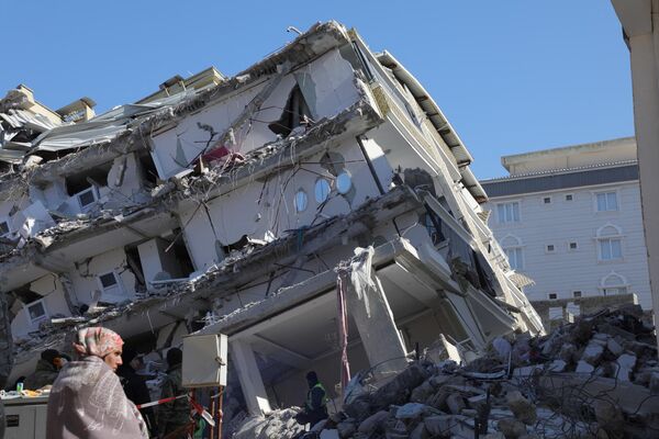 یک زن در 11 فبروری 2023، پنج روز پس از زلزله 7.8 ریشتری که منطقه مرزی ترکیه و سوریه را لرزاند، در مقابل یک ساختمان فروریخته در اصلاحیه، در منطقه سخت آسیب دیده غازیانتپ ایستاده است.(عکس از زین الریفای / خبرگزاری فرانسه) - اسپوتنیک افغانستان  