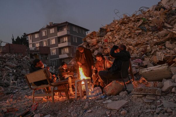 ساکنان محلی که عزیزانشان هنوز زیر آوار هستند، یک هفته پس از زلزله 7.8 ریشتری که بخش‌هایی از ترکیه و سوریه را لرزاند، در کنار ساختمان‌های فروریخته دور آتش جمع می‌شوند.این عکس در هاتای در 14 فبروری 2023، گرفته شده است.(عکس از بولنت کیلیچ / خبرگزاری فرانسه) - اسپوتنیک افغانستان  