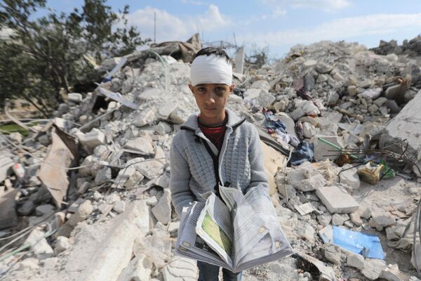 یک پسر سوری که خانواده خود را از دست داده و همچنین در اثر زلزله مرگبار ترکیه و سوریه مجروح شده است، کتابی را در حالی که در میان آوار خانه خانوادگی خود در شهر جیندایریس در منطقه تحت کنترل شورشیان ایستاده است حمل می کند.این عکس در شهر حلب سوریه در تاریخ 11 فبروری سال 2023 گرفته شده است. - اسپوتنیک افغانستان  