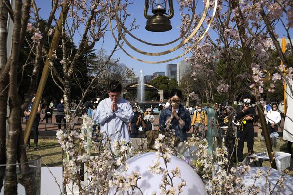  مرد و زنی پس از گذاشتن گل در مقابل بنای یادبود قربانیان دوازدهمین سالگرد زلزله عظیم، سونامی و فاجعه هستوی در پارک هیبیا در توکیو، دعا می‌کنند. - اسپوتنیک افغانستان  