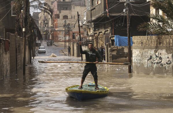 یک مرد فلسطینی سوار بر تخته پارویی در خیابانی سیل زده بر اثر باران شدید در اردوگاه آوارگان الشطی در نوار غزه20 مارچ 2023 - اسپوتنیک افغانستان  