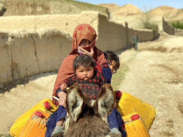 یک زن افغانستانی با فرزندانش در 25 مارچ 2023 در حالی که در امتداد خیابانی در ولسوالی زری ولایت بلخ، سوار بر خر.(عکس از عاطف آریان / خبرگزاری فرانسه) - اسپوتنیک افغانستان  