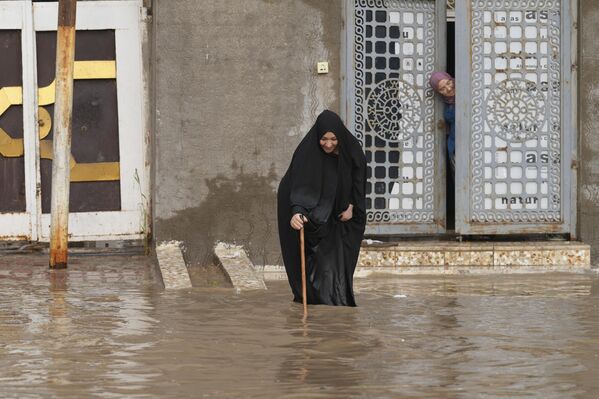 در پی بارش شدید باران در شهر نجف اشرف عراق، یک زن در سیلاب در خیابانی راه می‌رود.26 مارچ 2023(عکس از قاسم الکابی / خبرگزاری فرانسه) - اسپوتنیک افغانستان  