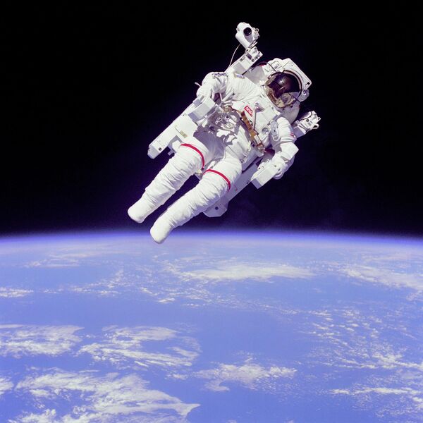 فضانورد Bruce McCandless II، متخصص ماموریت، در یک فعالیت خارج از وسیله نقلیه (EVA)، چند متر دورتر از کابین شاتل فضایی چلنجر. او از یک واحد مانور سرنشین دار با پیشرانه نیتروژنی (MMU) استفاده می کند. او این EVA را بدون اتصال به شاتل انجام می دهد. تصویر نمای ابری از زمین را در پس زمینه نشان می دهد. - اسپوتنیک افغانستان  