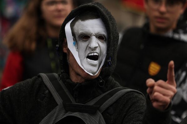 یک معترض که ماسکی شبیه به رئیس‌جمهور فرانسه بر سر دارد، هنگام شرکت در تظاهرات روز اول ماه مه (روز کارگر) به مناسبت روز جهانی کارگران. بوردو، جنوب غربی فرانسه، اول مه 2023. - اسپوتنیک افغانستان  