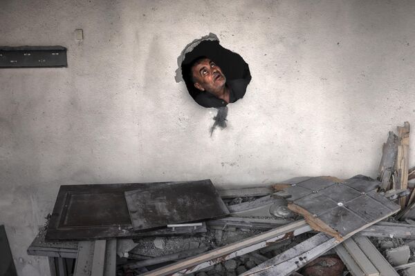 مردی در 13 می 2023 از سوراخی در میان آوارهای ساختمانی که در جریان حمله هوایی اسرائیل در دیرالبلاح در مرکز نوار غزه مورد اصابت قرار گرفته است نگاه می کند. - اسپوتنیک افغانستان  