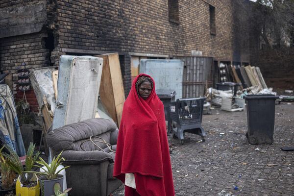 زنی در ژوهانسبورگ آفریقای جنوبی در کنار ساختمانی مخروبه که به عنوان سرپناه استفاده می شود خود را با پتویی می پوشاند. - اسپوتنیک افغانستان  