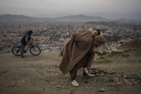 عبدالقادر قاضی زاده، 61 ساله، در حالی که پسرش احمد سر، 2 ساله را حمل می کند، سنگ ها را از جاده جدا می کند تا دوچرخه ها و اتومبیل ها در محله Tape TV در کابل، افغانستان، یکشنبه، 28 می 2023 بهتر تردد کنند. - اسپوتنیک افغانستان  
