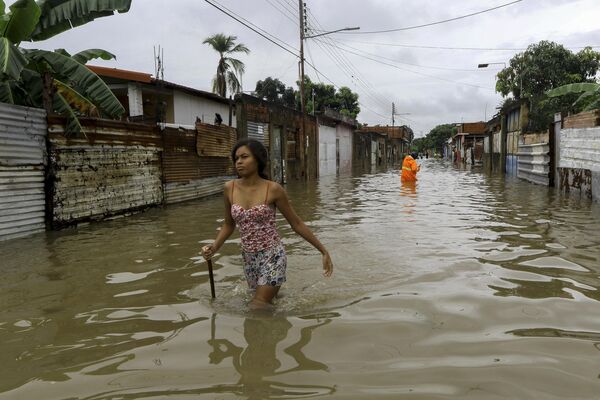 زنی در حال عبور از یک جاده سیل‌زده در حالی که پرسنل حفاظت مدنی به دنبال تخلیه مردم هستند پس از باران‌های شدید ناشی از امواج گرمسیری که چندین جامعه در شهر والنسیا، ایالت کارابوبو، ونزوئلا، در 30 می 2023 تحت تاثیر قرار داد. - اسپوتنیک افغانستان  