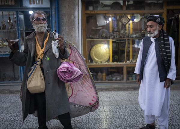 یک مرد به یک بی خانمان نگاه می کند که با پیاده روها در مرکز شهر هرات، افغانستان صحبت می کند. - اسپوتنیک افغانستان  