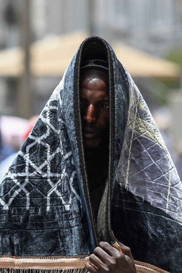 یک زائر مسلمان هنگام قدم زدن در شهر مقدس مکه در حالی که مسلمانان از سراسر جهان برای زیارت سالانه حج وارد می شوند، از یک سجاده (جای نماز) برای محافظت از خود در برابر خورشید استفاده می کند.23 جون 2023 - اسپوتنیک افغانستان  