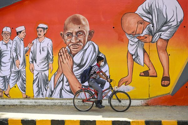 پسری با دوچرخه از کنار نقاشی دیواری مهاتما گاندی نماد استقلال هند در دهلی نو می‌گذرد.6 آپریل 2022(عکس از سجاد حسین / خبرگزاری فرانسه) - اسپوتنیک افغانستان  