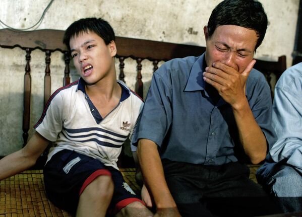 نگوین ون کوی، 49 ساله، در جولای 2004 در حالی که با پسرش نگوین کوانگ ترانگ، 17 ساله، در خانه اش در های فونگ، ویتنام نشسته، گریه می کند.کوی معتقد است که نقص مادرزادی فرزندانش توسط ماده نارنجی، ایجاد شده است که او در طول جنگ ویتنام در معرض آن قرار گرفته است. - اسپوتنیک افغانستان  