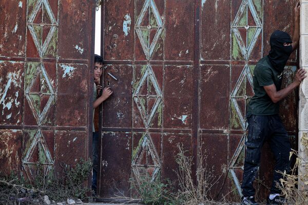 در 21 آگوست ، 2023در حالی که یک جوان فلسطینی نقابدار هنگام درگیری با نیروهای اسرائیلی ایستاده است و سربازان در حال انجام عملیات جستجو در قریه ی بیته در کرانه باختری اشغالی هستند، یک پسر از پشت دروازه نگاه می کند. - اسپوتنیک افغانستان  