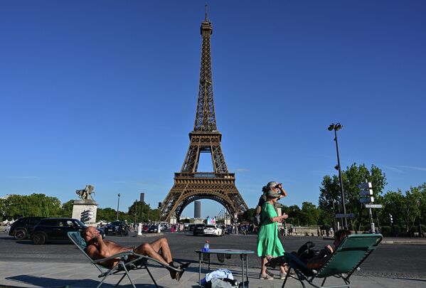 در 21 آگوست 2023، رهگذران از کنار دو نفر می گذرند که روی یک صندلی بلند در مقابل برج ایفل در پاریس از نور خورشید لذت می برند، در حالی که هشدار موج گرمای قرمز در چهار بخش فعال شده است، که نشانه ای از یک قسمت &quot;طولانی&quot; است که 49 بخش را نیز تحت تاثیر قرار داده است.ده‌ها میلیون نفر در فرانسه در اثر موج گرمای اواخر تابستان در 21 آگوست 2023 به ستوه آمدند، همچنان با دمای بی‌سابقه در منطقه دره رون که در حال رشد است و آتش‌سوزی جنگلی نیز در جنوب شرقی شعله‌ور شد. - اسپوتنیک افغانستان  