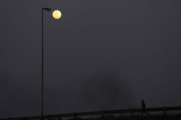 یک ابرماه در آسمان در حالی که مردی در خیابان می دود، در وسلوروس، شرق ژوهانسبورگ، افریقای جنوبی، چهارشنبه، 30 اگوست 2023 دیده می شود.   30 اگوست دومین ابرماه ماه را می بیند، زمانی که یک ماه کامل به لطف موقعیت کمی نزدیکتر به زمین، کمی بزرگتر و درخشان تر به نظر می رسد. (نگاره از تیمبا هدیبه آسوشیتد پرس) - اسپوتنیک افغانستان  