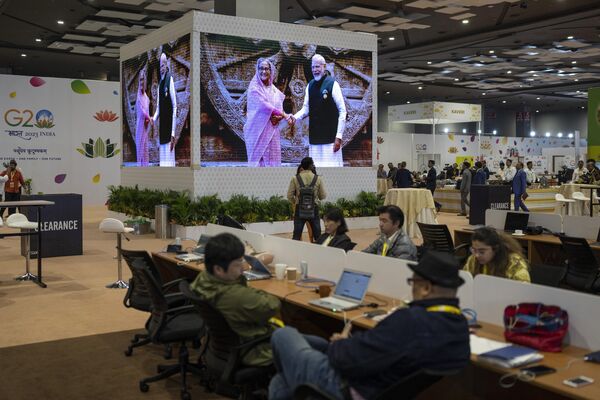 روزنامه‌نگاران در مرکز رسانه‌های بین‌المللی کار می‌کنند و تصاویر زنده روی یک صفحه نمایش بزرگ نشان می‌دهند که نارندرا مودی، نخست‌وزیر هند، از شیخ حسینه، نخست‌وزیر بنگلادش در مرکز همایش بهارات مانداپام برای اجلاس سران G20 در دهلی نو، هند، شنبه، 9 سپتامبر 2023 استقبال می‌کند. - اسپوتنیک افغانستان  